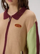Campera estilo bomber Mutma Satifo, de diseño colorblock con cuerpo en color óxido y mangas celestes con detalles en azul marino. Cuenta con cuello camisero, cierre frontal, puños y ruedo elásticos rayados, y un parche gráfico en el pecho.