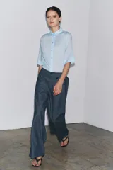 Camisa de color mostaza, con cuello solapa, manga corta y bajo recto. Cierre frontal con botones.