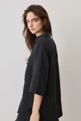 Camisa negra de manga corta, con cuello camisero, cierre frontal de botones y un bolsillo aplicado en el pecho.