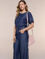 Cartera bandolera estructurada de eco cuero rosado con textura graneada, silueta curva y cierre superior. Posee correa larga regulable con detalles de cadena dorada, bolsillo frontal con logo metálico, pañuelo estampado a contratono anudado en un lateral y base rígida con apoyos metálicos.