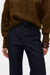 Jean de tiro alto con corte acampanado desde la rodilla. Presenta un diseño de denim oscuro con pliegues frontales y traseros, cierre con botón oculto y bolsillos traseros decorativos.