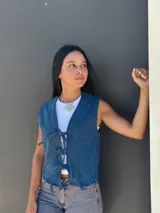 Chaleco de jean azul con cierre frontal mediante lazos ajustables, sin mangas y corte recto.