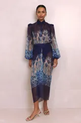 Camisa de organza semitransparente con estampado de plumas de pavo real en tonos azules y cuello doble. Cuenta con mangas abullonadas con abertura y puños cerrados con botón. Incluye hombreras.