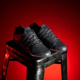 Championes urbanos Adidas Adiracer L en colaboración con Audi Revolut F1 Team, de color negro con detalles en rojo. Diseño de inspiración automovilística con las clásicas tres tiras en los laterales, suela de perfil bajo y el logo de la marca en la lengüeta y el talón.