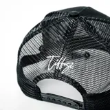 Gorra tipo trucker color negro con panel frontal rígido y parte trasera de malla. Presenta un bordado frontal en color blanco con el logo de la marca.