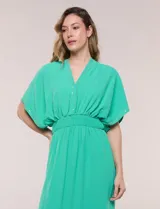 Vestido largo amarillo de corte fluido con escote en V, mangas cortas amplias y apliques de tachas en el escote y puños. Posee cintura elastizada fruncida y falda larga con tajos laterales en el ruedo.