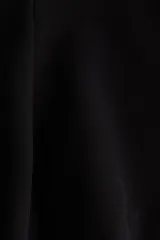 Top sin mangas con escote bote, costuras moldeadoras y pliegues en la cintura que forman un peplum acampanado. Cuenta con cierre oculto en la espalda y diseño de corte sastre en color negro.