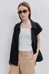 Chaleco de jean negro, de calce relajado con hombros caídos, cuello camisero, cierre frontal con botones y grandes bolsillos aplicados.