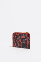 Monedero de estructura rígida con acabado brillante, cierre de cremallera y logo metálico frontal. Presenta un diseño de animal print en tonos rojos y negros.
