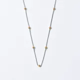 Cadena plateada con eslabones finos y pequeñas cuentas doradas distribuidas a lo largo de la cadena.