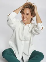 Camisa blanca de corte oversize, con cuello clásico, cierre frontal con cartera oculta y bolsillo delantero. Presenta mangas largas con puños abotonados.