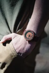 Reloj de pulsera con caja, esfera y malla de madera de sándalo rojo, con marcadores y manecillas negras. Presenta un diseño circular con corona lateral.