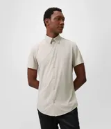 Camisa de manga corta color beige, con cuello camisero, cierre frontal de botones y diseño liso.