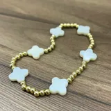Pulsera elástica de baño dorado con cuentas esféricas metálicas y dijes de nácar en forma de trébol.