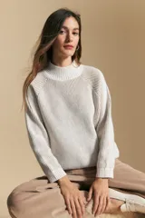 Polera de tejido acanalado en color blanco con sutiles líneas verticales en tono beige. Presenta cuello alto, mangas largas con corte raglán y puños acanalados.