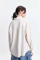 Camisa oversize color crema con detalles de puntilla roja en el frente.