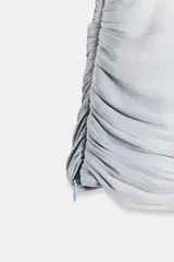 Camisa de escote en pico con lazada frontal en el mismo tejido, manga larga con puños y bajo drapeado. Presenta un acabado satinado y cierre lateral con cremallera oculta.