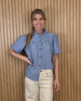 Camisa de manga corta azul melange, con cuello alto con volados, cierre frontal de botones y detalles fruncidos en el canesú y los puños.
