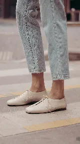 Zapato de cuero marrón chocolate con cordones finos negros, punta cuadrada y detalles de perforaciones decorativas en los laterales.