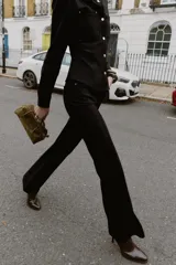 Camisa entallada color marrón oscuro, con cuello camisero y manga larga. Presenta dos bolsillos de plastrón en el delantero y cierre frontal con botones a presión dorados.