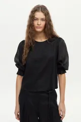 Blusa de lino blanca con escote redondo y mangas cortas abullonadas con detalles de volados en los puños.
