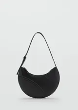 Bolso de hombro tipo media luna en color negro, con diseño minimalista y detalles de costuras decorativas perforadas en la parte frontal. Cuenta con una correa ajustable con hebilla y cierre superior.