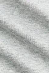 Buzo en tejido liviano color gris melange, con cuello camisero, tapeta con botones frontales, hombros caídos y puños acanalados.