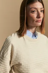 Sweater color crema con mangas abullonadas y puños elastizados. Presenta una textura tejida en relieve con patrón de ladrillos en el cuerpo y rayas horizontales en las mangas.