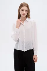 Camisa negra de poliéster con detalles de lurex y textura en relieve, corte holgado, mangas largas con puños y cierre frontal con botones.