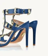Sandalias de tacón alto color azul con textura de piel de serpiente y apliques de tachas piramidales doradas.