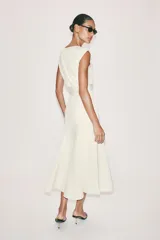 Vestido midi de crepe color blanco marfil, sin mangas, con cuello redondo y corte en la cintura. Falda con vuelo evasé y cierre lateral con cremallera oculta.