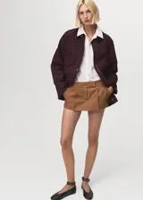Parka color bordó, de corte recto, con cierre frontal de cremallera y botones a presión. Presenta cuello camisero de pana, bolsillos frontales de parche con solapa y mangas largas con puños ajustables. Incluye forro interior.