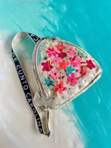 Mochila Kiri de cuero natural de la marca Carolina De Cunto, con diseño artístico pintado a mano de flores multicolores en el frente. Cuenta con una correa bandolera negra con el nombre de la marca en letras blancas y cierre superior con cremallera.