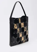 Bolso tipo shopper de diseño patchwork, confeccionado mediante tiras entrelazadas de cuero negro liso y cuero con estampado de serpiente, unidas por anillas metálicas plateadas. Cuenta con un asa de hombro fija y cierre magnético.