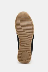 Zapatilla deportiva tipo running con diseño de paneles en contraste. Presenta cuerpo en color negro con refuerzos de gamuza sintética, detalle de pespuntes, talón en color crema y suela dentada bicolor.