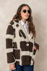 Chaqueta oversize con diseño de cuadros en relieve, confeccionada en una combinación de lana y poliéster con textura tipo borreguillo. Presenta un corte holgado, cuello con solapas y un botón joya central.