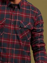Camisa de franela a cuadros azules y grises, de manga larga con puños abotonados y dos bolsillos frontales con solapa abotonada.