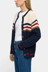 Saco tejido de punto con diseño de bloques de color en azul marino, crema, rojo y marrón. Presenta cierre frontal con botones, cuello redondo y textura de cableado en el tejido.