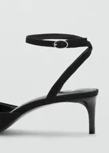 Zapato tipo kitten heel color negro, con punta fina y detalle de pompones en el empeine. Cuenta con una tira ajustable con hebilla en el tobillo.