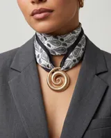 Pañuelo de seda blanco y negro con estampado paisley, bordes negros y un dije dorado en forma de espiral.