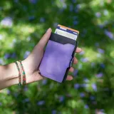 Billetera tarjetero automática con estructura de aluminio y revestimiento de cuero bicolor en tonos verde oliva y beige. Cuenta con un cierre de broche a presión y el logo de la marca grabado en la parte inferior.