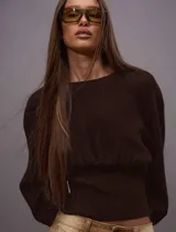 Sweater de tejido de punto color chocolate, con diseño de mangas amplias y cintura ajustada con elástico ancho. Presenta un corte relajado en la parte superior y un ajuste ceñido en la cintura que estiliza la silueta.
