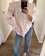 Camisa de algodón color rosado, de corte holgado, con cuello clásico, cierre frontal con botones y mangas largas abullonadas con detalles fruncidos.
