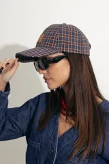Gorra tipo baseball con estampado de cuadros escoceses en tonos azul, naranja y beige. Presenta un parche de cuero sintético en el frente y cierre ajustable en la parte posterior.