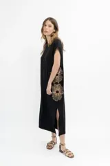 Vestido largo negro, sin mangas, de corte recto y holgado, con abertura lateral. Presenta un bordado grande de flores estilizadas en color dorado/naranja en el lateral derecho.