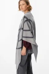 Ruana de tejido de punto con diseño geométrico de líneas curvas en tonos beige y visón. Presenta una caída fluida y envolvente, ideal para usar como capa sobre otras prendas.