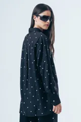 Camisa de corte clásico con estampa de lunares blancos sobre fondo negro, manga larga con puños abotonados y bolsillo frontal.