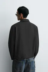 Camisa negra de corte relaxed fit, con cuello solapa y cierre frontal de botones, manga larga con puños abotonados y sutil patrón geométrico en jacquard.