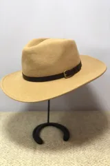 Sombrero de ala ancha confeccionado en lana color beige, con detalle de cinta de cuero marrón y hebilla metálica.