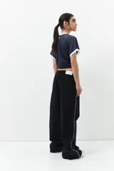 Pantalón de jean ancho color negro, de tiro bajo y confeccionado en algodón. Cuenta con una línea bordada color marrón en ambas piernas y cinco bolsillos.